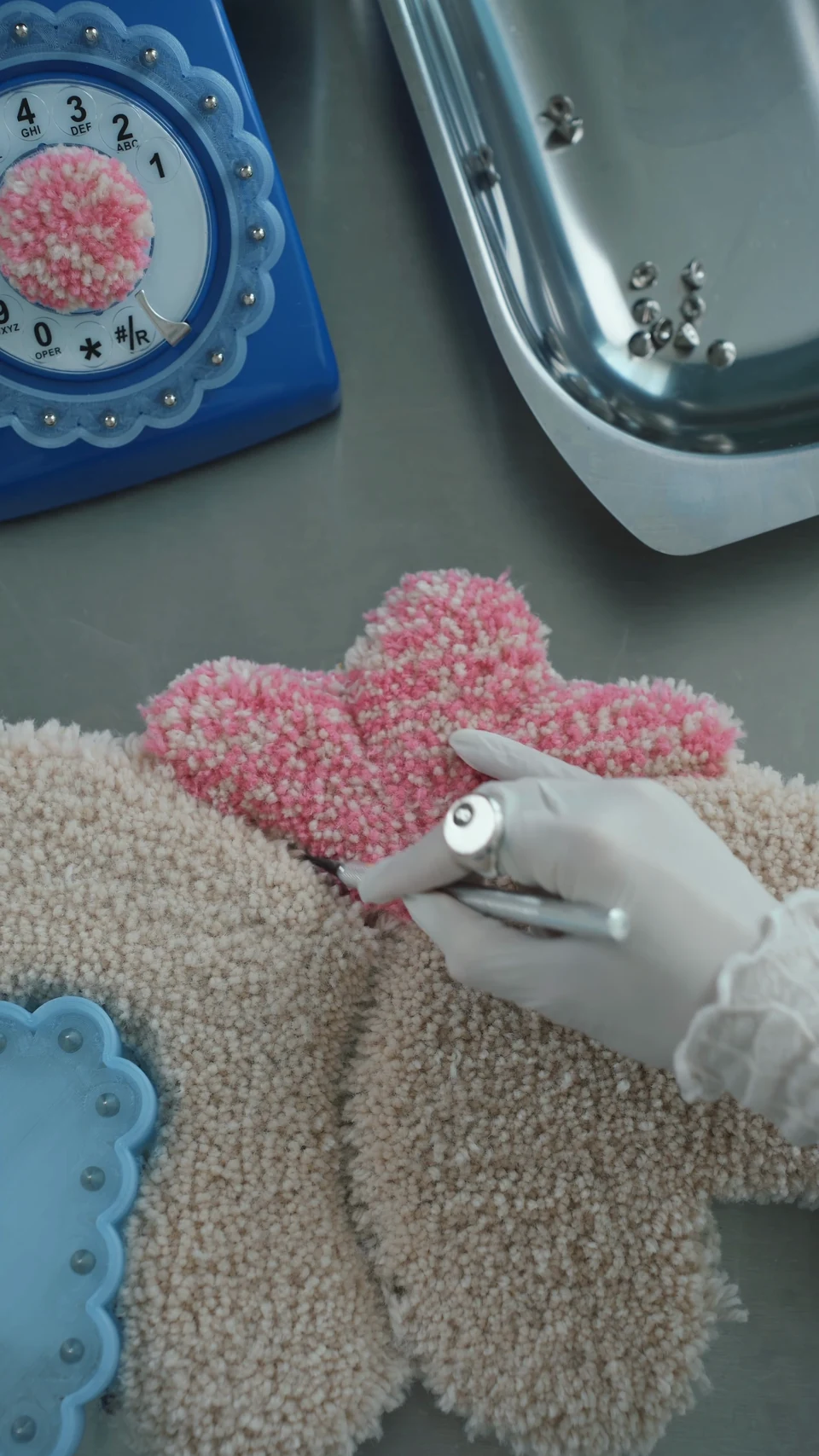 A hand trimming the pink tufted surface of the Receiver mirror frame.