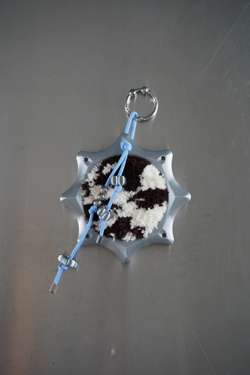 The sculptural silver-grey charm with brown and cream tufting, blue cord and metal clip.